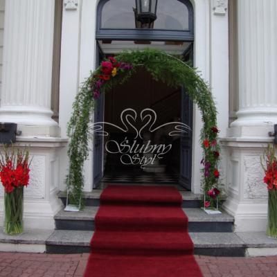 Czerwone gladiole, łuk kwiatowy w towarzystwie czerwonego dywanu na wejściu do budynku