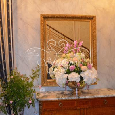 Dekoracyjna misa na nóżce z hortensjami i storczykami na komodzie  