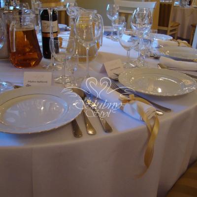 Białe serwetki na stołach przewiązane złotą wstążeczką 
