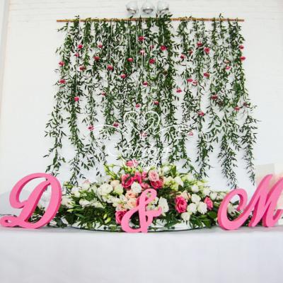 Różowe inicjały na stole Pary Młodej - w tle ścianka ślubna