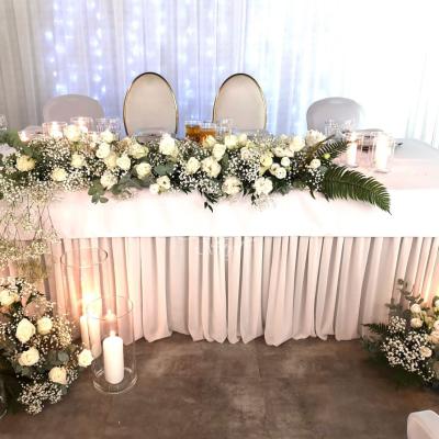 Kompozycja z białych kwiatów z dodatkiem zieleni na stole Młodej Pary