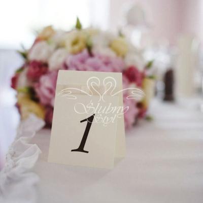 Numerek stołu na sali weselnej - w tle kompozycja kwiatowa