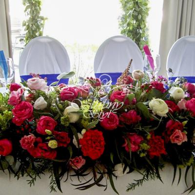 Ostróżka, angielskie róże i jaskry w kompozycji na stole przed Młodą Parą