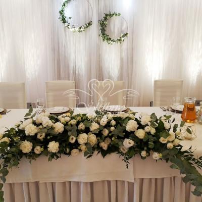 Złote obręcze z żywymi kwiatami i zielenią na ściance za młodymi